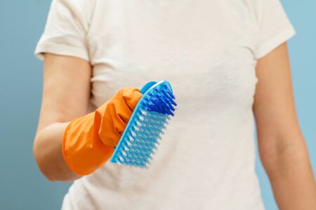 Woman in a white t-shirt holding a plastic brush on the blue background. Washing and cleaning concept.の写真素材