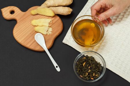 Health remedy foods for cold and flu relief. Female hand with a cup of tea and ginger on a black background. Top view. Foods That Boost the Immune System.の写真素材