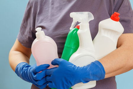 Woman in a t-shirt holding plastic bottles of washing liquid on the blue background. Washing and...