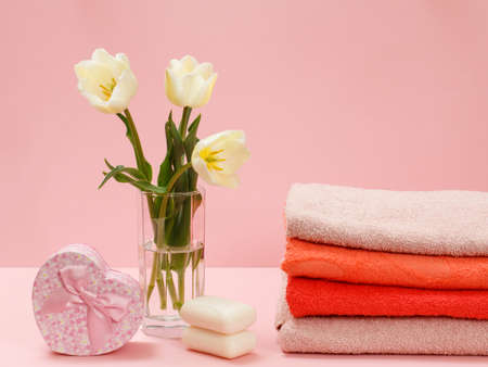 Bouquet of yellow tulips in a glass vase, a gift box, soup and stacked towels on a pink background.の写真素材