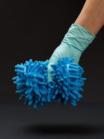 Hand in a nitrile glove holding a rag on the black background. Washing and cleaning concept.