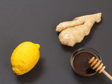 Health remedy relief foods for cold and flu with lemon, ginger and honey on a black background. Top...