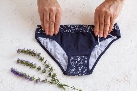 Women's hands holding beautiful cotton panties on the white structured background. Woman underwear...