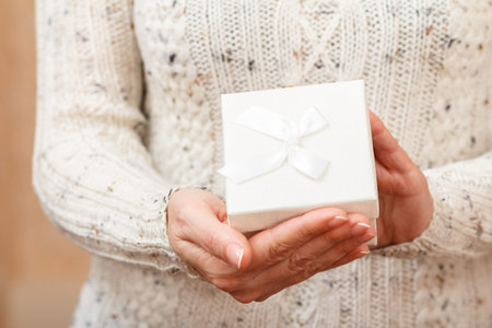 Woman holding a white gift box in her hands. Shallow depth of field, Selective focus on the box. Concept of giving a gift on holiday or birthday.の写真素材