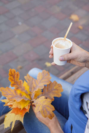 Close-up view of young woman with a cup of coffee and dry autumn leaves in her hands. Top view. Autumn composition.の写真素材