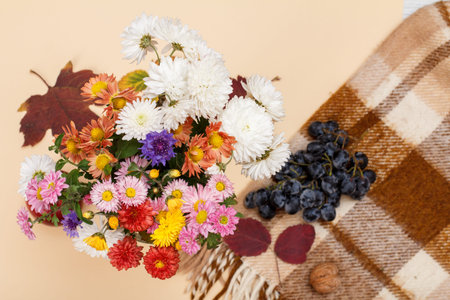 Big bouquet of colorful different flowers and a checkered plaid with grapes on the beige background....