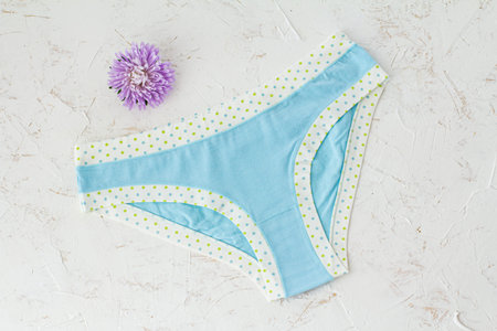 Blue cotton panties with a flower bud on the white structured background. Woman underwear set. Top...