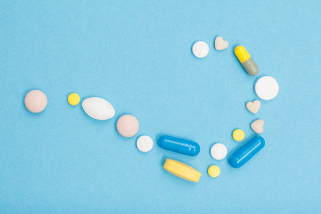 Different pills and capsules in the form of a question mark sign on the blue background with copy space. Top viewの写真素材