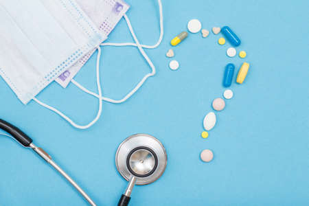 Pills and capsules in the form of a question mark sign, a phonendoscope and medical face masks on the blue backgroundの写真素材