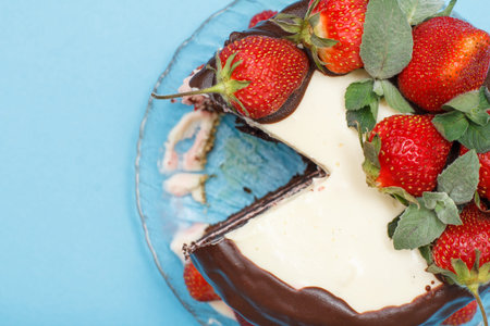 Homemade chocolate cake decorated with fresh strawberries on a glass plate on the blue background....