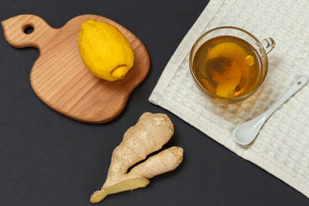 Health remedy foods for cold and flu relief. Cup of tea and lemon, ginger on a black background. Top view. Foods That Boost the Immune System.の写真素材