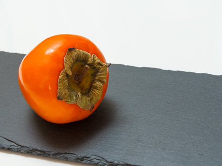 Delicious ripe persimmon fruit on the black stone cutting board. Organic fruits.の写真素材