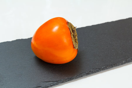 Delicious ripe persimmon fruit on the black stone cutting board. Organic fruits.の写真素材