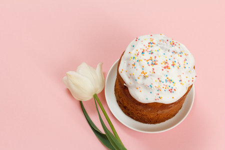 Easter cake on a plate with a tulip flower on the pink background. Traditional orthodox christian...