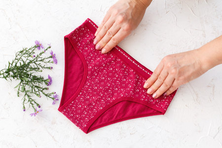Women's hands holding beautiful red cotton panties on the white structured background. Woman...