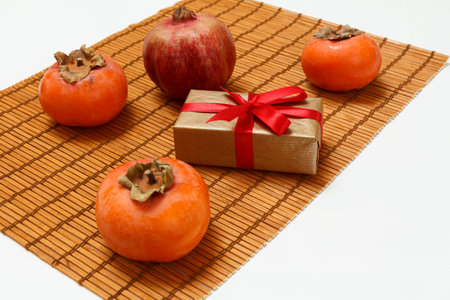Delicious ripe persimmon and a pomegranate fruits with a gift box on the bamboo napkin. Organic fruits.の写真素材