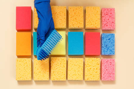 Sponges of different colors and a hand in a rubber glove with a plastic brush on the beige background. Top view. Washing and cleaning set.の写真素材