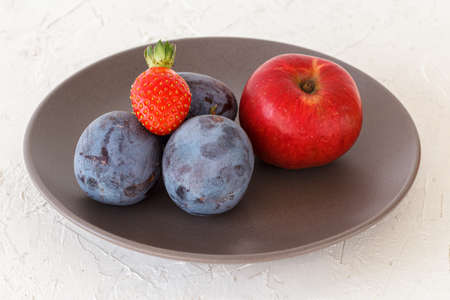 Picked ripe plums, an apple, a strawberry on the plate. Just harvested fruits.の写真素材