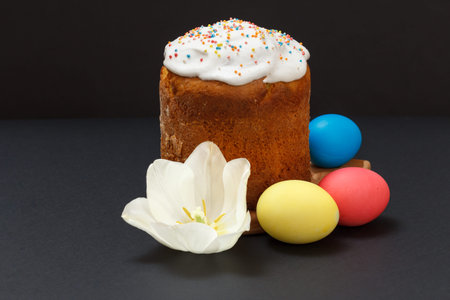 Sweet Easter cake, colored Easter eggs with a tulip flower bud on the black background.