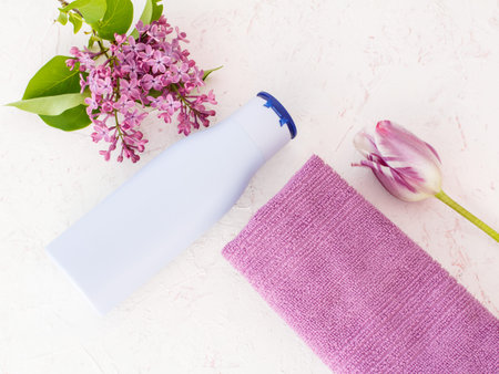 Bottle of shampoo, a towel, tulip and lilac flowers on the structured background. Women's cosmetics...
