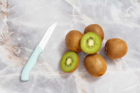 Whole and sliced kiwi fruits and a kitchen ceramic knife on the kitchen stone table. Healthy food. Top view.の写真素材