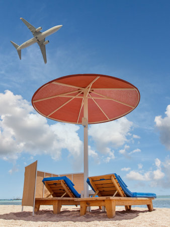Beach with an umbrella and sunbeds on a seashore with flying airplane in the sky. Summer time holidays concept.の写真素材