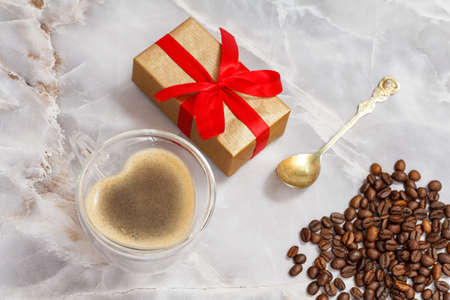 Glass cup of coffee, a spoon, a gift box and roasted coffee beans on the kitchen table. Top view.の写真素材