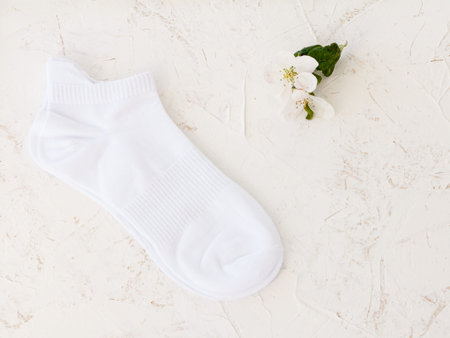 Pair of white women socks and flowers of an apple tree on the white structured background, Top view.
