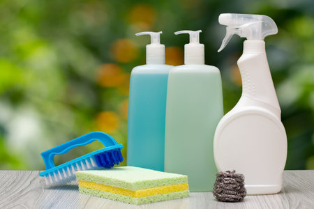 Three blastic bottles of dishwashing liquid, glass and tile cleaner, a brush, a sponge on the...