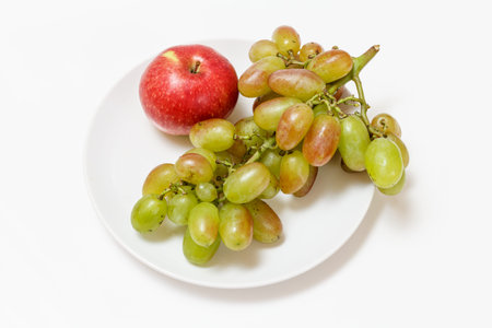 Bunch of green grapes and apple on white plate.