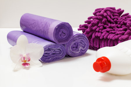 Plastic bottle of washing liquid, garbage bags, a rag and a white orchid flower on a tiled floor. Washing and cleaning set.の写真素材