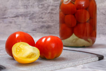 Tomatoes fresh and preserved in a glass jar. Pickled tomatoes on the gray background. Homemade preserves.の写真素材