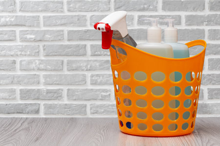Plastic basket with bottles of dishwashing liquid, glass and tile cleaner, detergent for microwave ovens and stoves with a brick wall on the background. Washing and cleaning concept.の写真素材