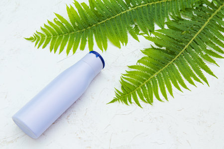 Bottle of shampoo and leaves of fern on the white structured background. Women's accessories for...