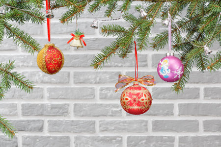 Branches of fir tree with balls, bells and other Christmas ornament with a brick wall on the...