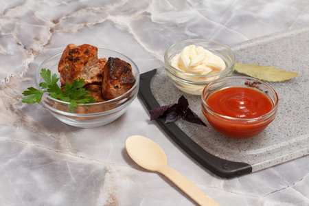 Grilled pork in a glass bowl with fresh basil. Porcelain bowls with ketchup and cheese sauce on the...