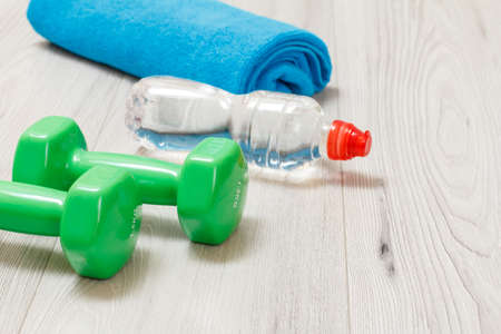 Green dumbbells for fitness, a bottle of water and a towel on the background.の写真素材