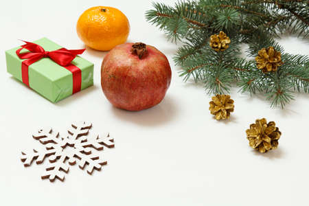 Natural fir tree branch with cones, a gift box, a tangerine and a pomegranate on the white backgroundの写真素材