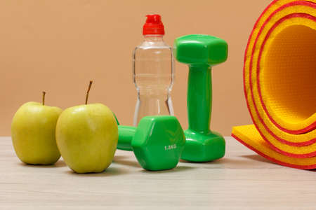 Dumbbells and a mat for fitness, a bottle of water and apples on the beige background.の写真素材