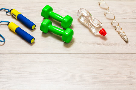 Skipping rope and dumbbells for fitness, a bottle of water and a tape-measure in a room or a gym on the gray floor. Top view.の写真素材