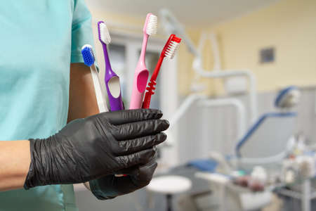 Close-up view of a dentist's hand with toothbrushes and a dental office on the background.の写真素材