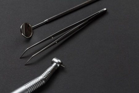 Head of high-speed dental handpiece with bur, a metal mirror and a tweezers on the black background....