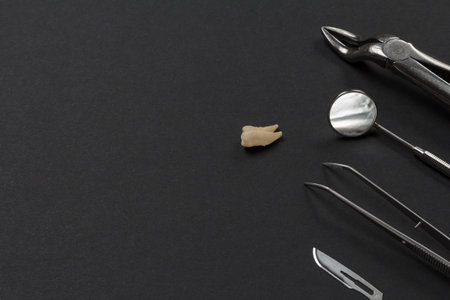 Stainless steel dental pliers, a mouth mirror, tweezers, a blade and an extracted sick tooth on the...