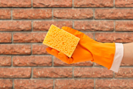 Womans hand in protective glove with sponge on beige background.