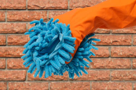 Close-up view of woman's hand in rubber protective glove with rag and a brick wall on the...