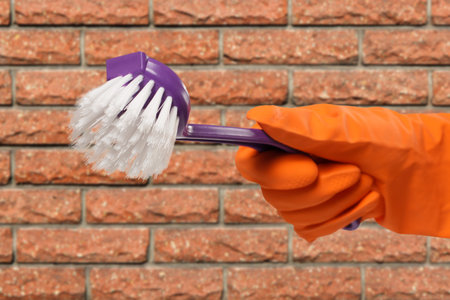 Close-up view of woman's hand in rubber protective glove with plastic brush and a brick wall on the...
