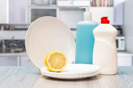 Plastic bottles of dishwashing liquid, glass and tile cleaner, clean plates and lemon at the kitchen. Washing and cleaning concept.の写真素材