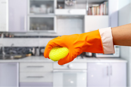 Woman's hand in orange protective glove with sponge at the kitchen. Washing and cleaning concept.