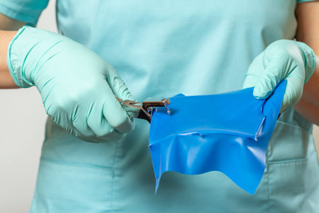 Dentists hands in gloves with dental punch and cofferdam scarf.