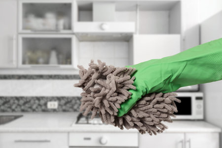 Close-up view of woman's hand in a rubber protective glove with the rag and the kitchen on the...